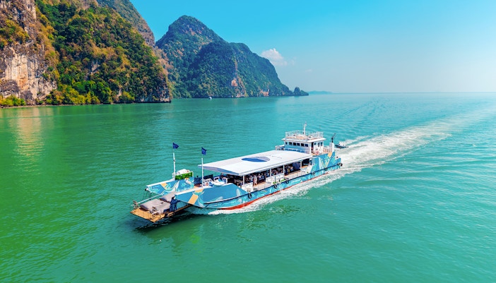 Cruise boat sailing in Phang Nga Bay with limestone cliffs in the background.