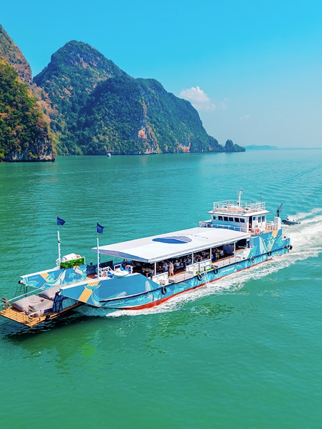 Cruise boat sailing in Phang Nga Bay with limestone cliffs in the background.