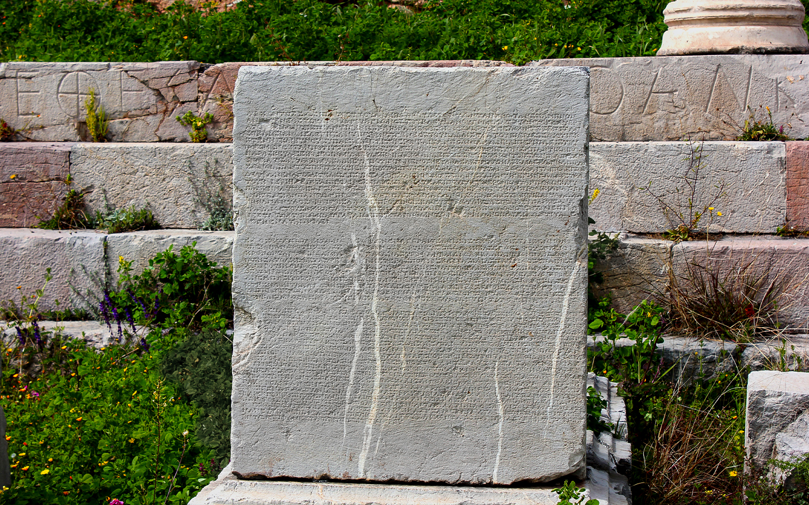 Ancient Greek inscription on stone at Delphi, Greece, surrounded by greenery.