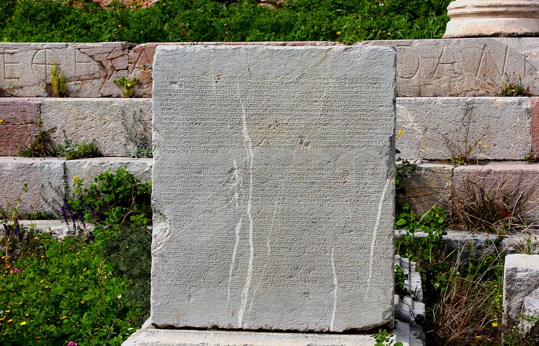 Ancient Greek inscription on stone at Delphi, Greece, surrounded by greenery.