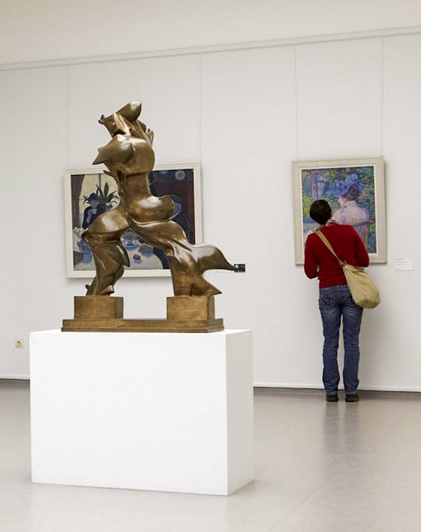 Bronze sculpture and visitor viewing paintings at Kröller Müller Museum.