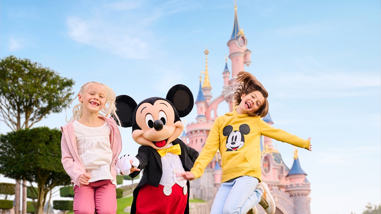 Mickey Mouse with two kids jumping in front of Sleeping Beauty Castle, Disneyland Paris.