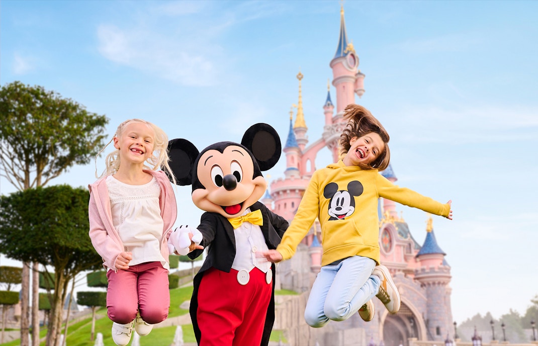 Mickey Mouse with two kids jumping in front of Sleeping Beauty Castle, Disneyland Paris.