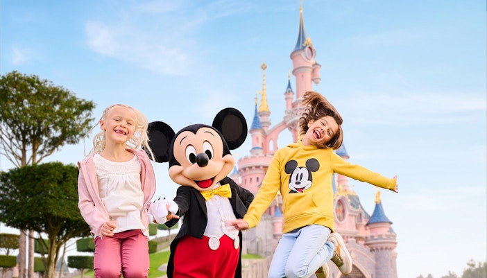 Mickey Mouse with two kids jumping in front of Sleeping Beauty Castle, Disneyland Paris.
