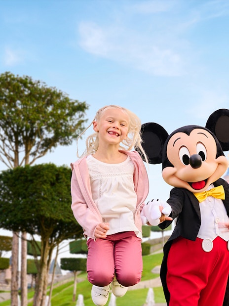 Mickey Mouse with two kids jumping in front of Sleeping Beauty Castle, Disneyland Paris.