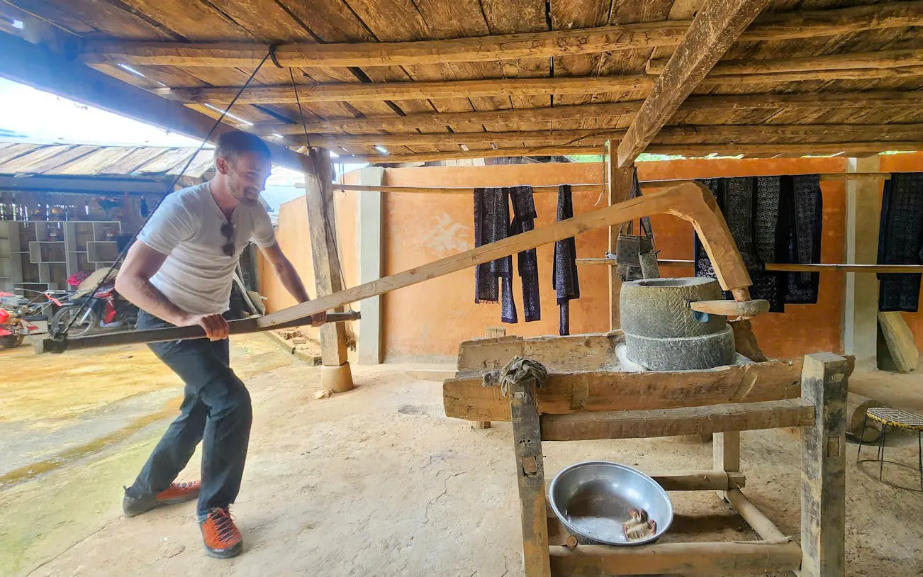 Man operating traditional rice mill in Mu Cang Chai village during trekking tour.