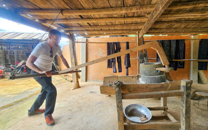 Man operating traditional rice mill in Mu Cang Chai village during trekking tour.