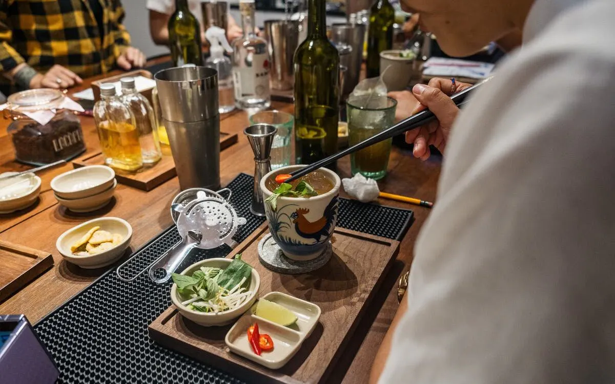 Person preparing Vietnamese coffee-themed cocktail with herbs and spices on a wooden table.