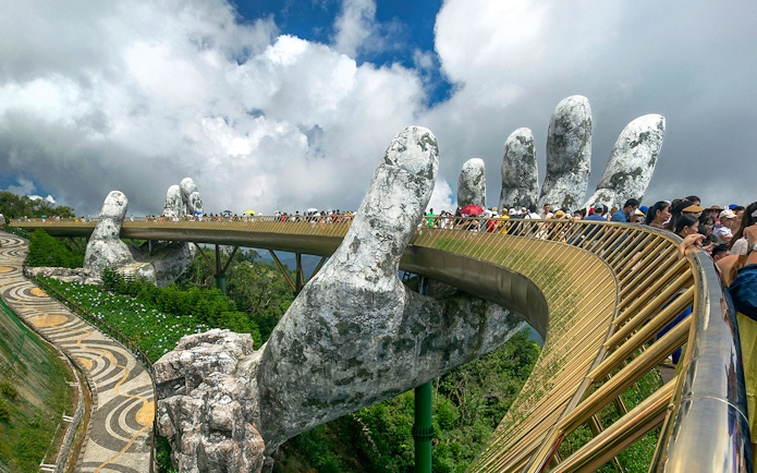 People walking on the Golden Bridge held by giant hands in Ba Na Hills, Vietnam.