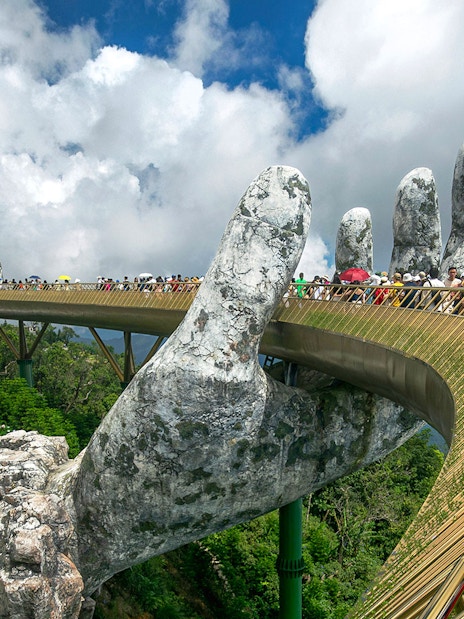 People walking on the Golden Bridge held by giant hands in Ba Na Hills, Vietnam.