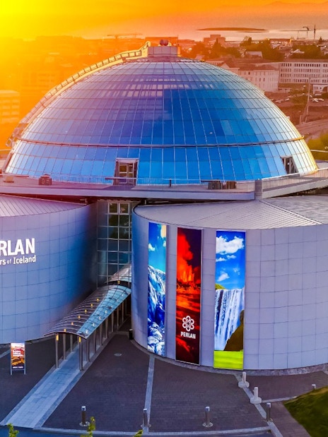 Aerial view of Perlan Museum's glass dome and exhibition halls in Reykjavik at sunset.