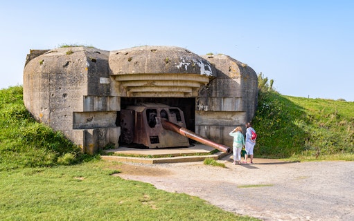 WWII Normandy bunker with tourists exploring, part of D-Day Beaches tour from Paris.