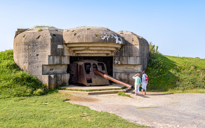 WWII Normandy bunker with tourists exploring, part of D-Day Beaches tour from Paris.