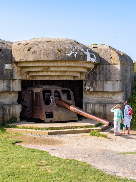 WWII Normandy bunker with tourists exploring, part of D-Day Beaches tour from Paris.