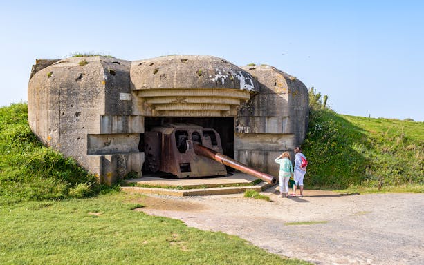 WWII Normandy bunker with tourists exploring, part of D-Day Beaches tour from Paris.