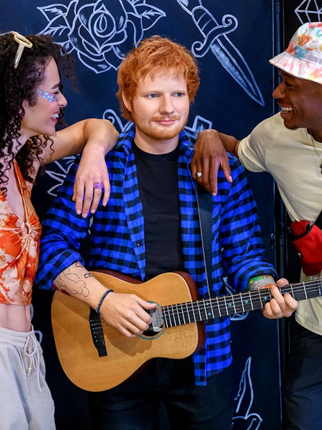Wax figure of a celebrity with guitar at Madame Tussauds London, surrounded by visitors.