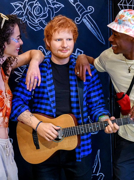 Wax figure of a celebrity with guitar at Madame Tussauds London, surrounded by visitors.