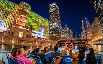 Chicago River cruise at night with city skyline and illuminated buildings.