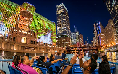 Chicago River cruise at night with city skyline and illuminated buildings.