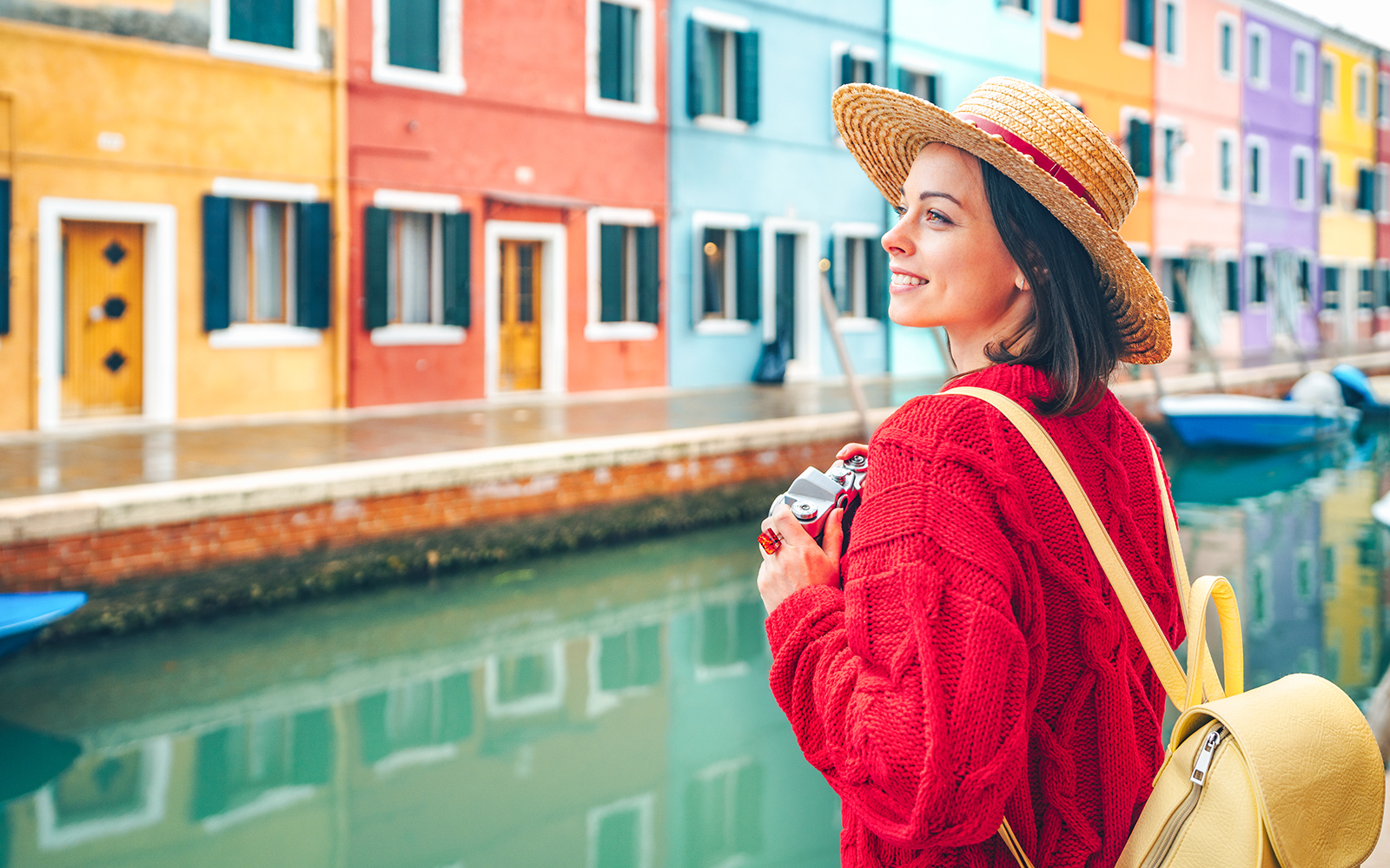 Tourist walking near vibrant, colorful houses along a canal in Burano, Italy.
