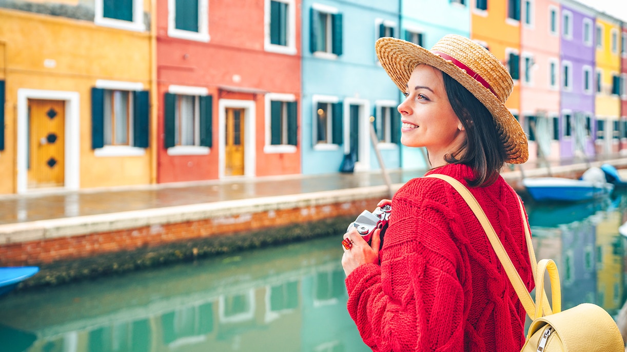 Tourist walking near vibrant, colorful houses along a canal in Burano, Italy.
