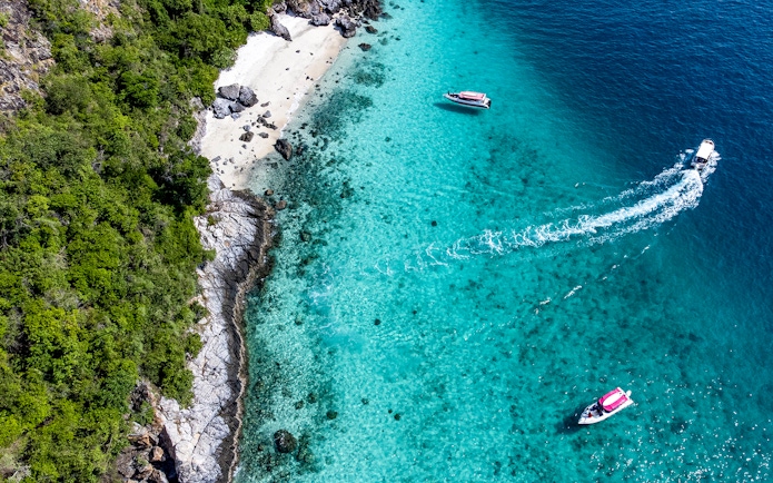 Aerial view of boats near the turquoise waters and rocky shore of Nemo Island, Pattaya.