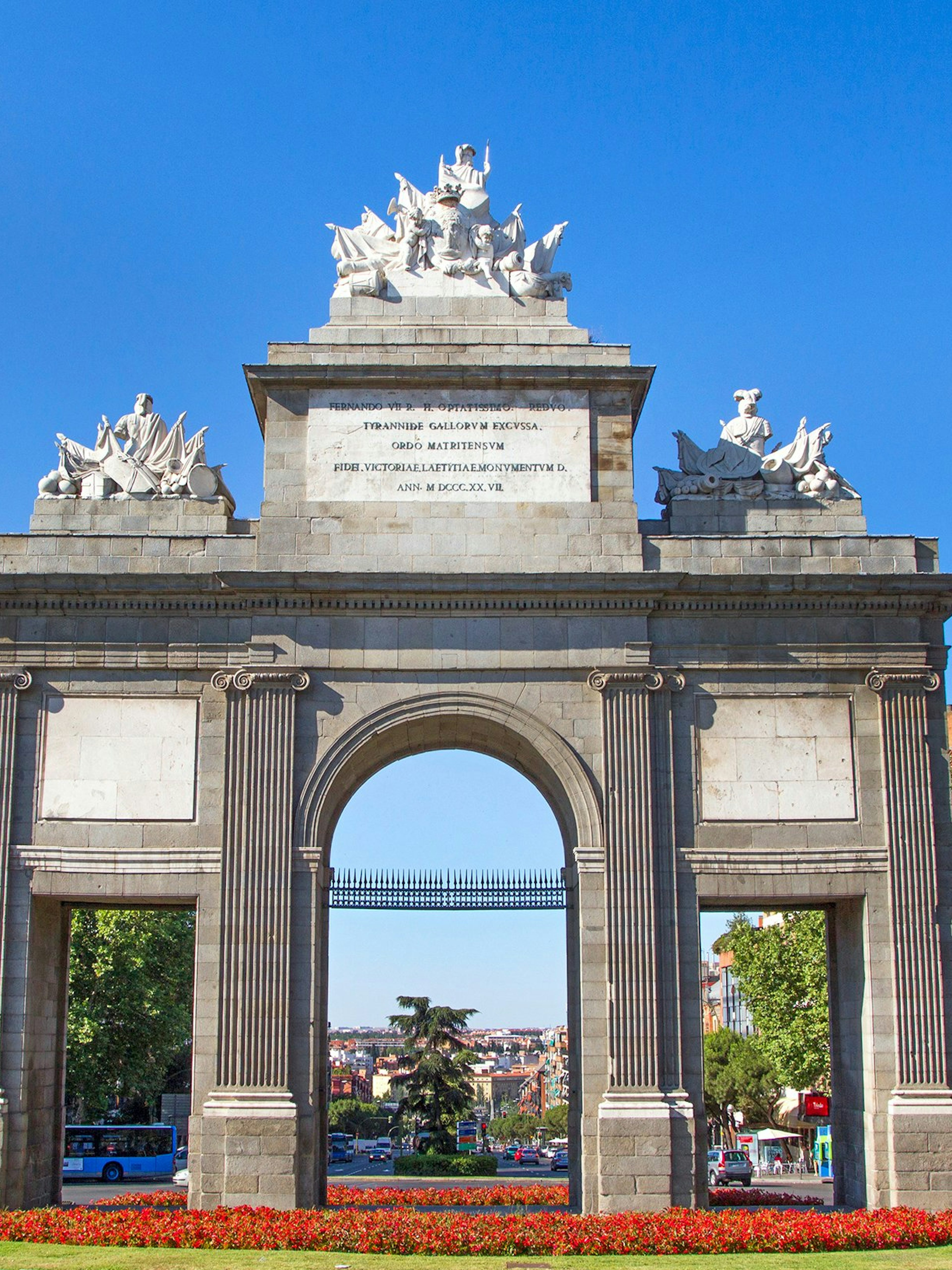 Puerta de Toledo arch in Madrid with sculptures and cityscape in the background.