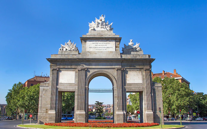 Puerta de Toledo arch in Madrid with sculptures and cityscape in the background.