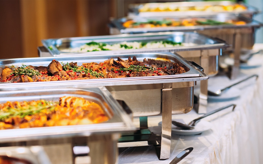 Buffet lunch with assorted dishes in stainless steel trays.