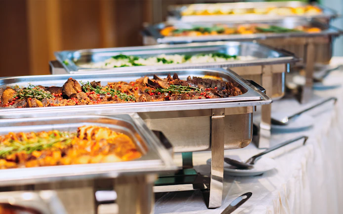 Buffet lunch with assorted dishes in stainless steel trays.