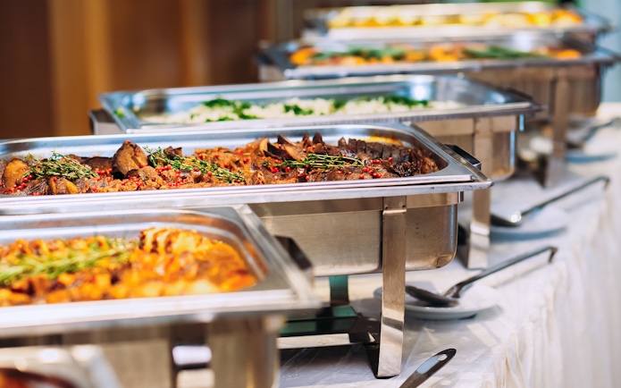 Buffet lunch with assorted dishes in stainless steel trays.
