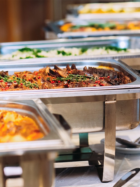 Buffet lunch with assorted dishes in stainless steel trays.
