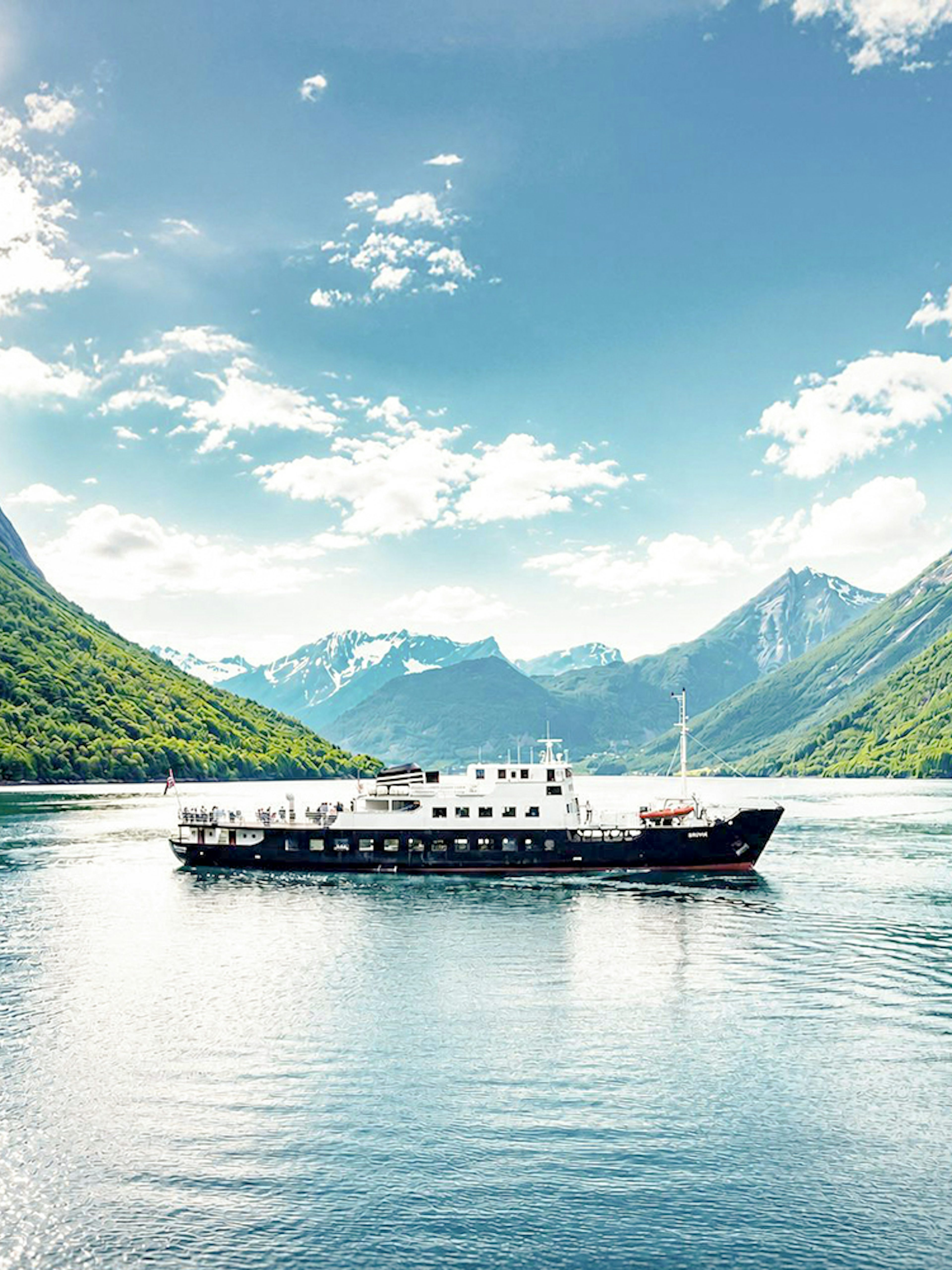 Boat cruising through Geiranger Fjord surrounded by lush mountains, Ålesund, Norway.