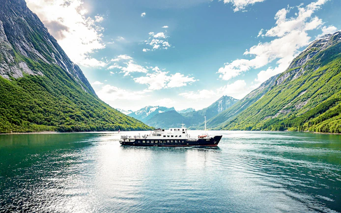 Boat cruising through Geiranger Fjord surrounded by lush mountains, Ålesund, Norway.