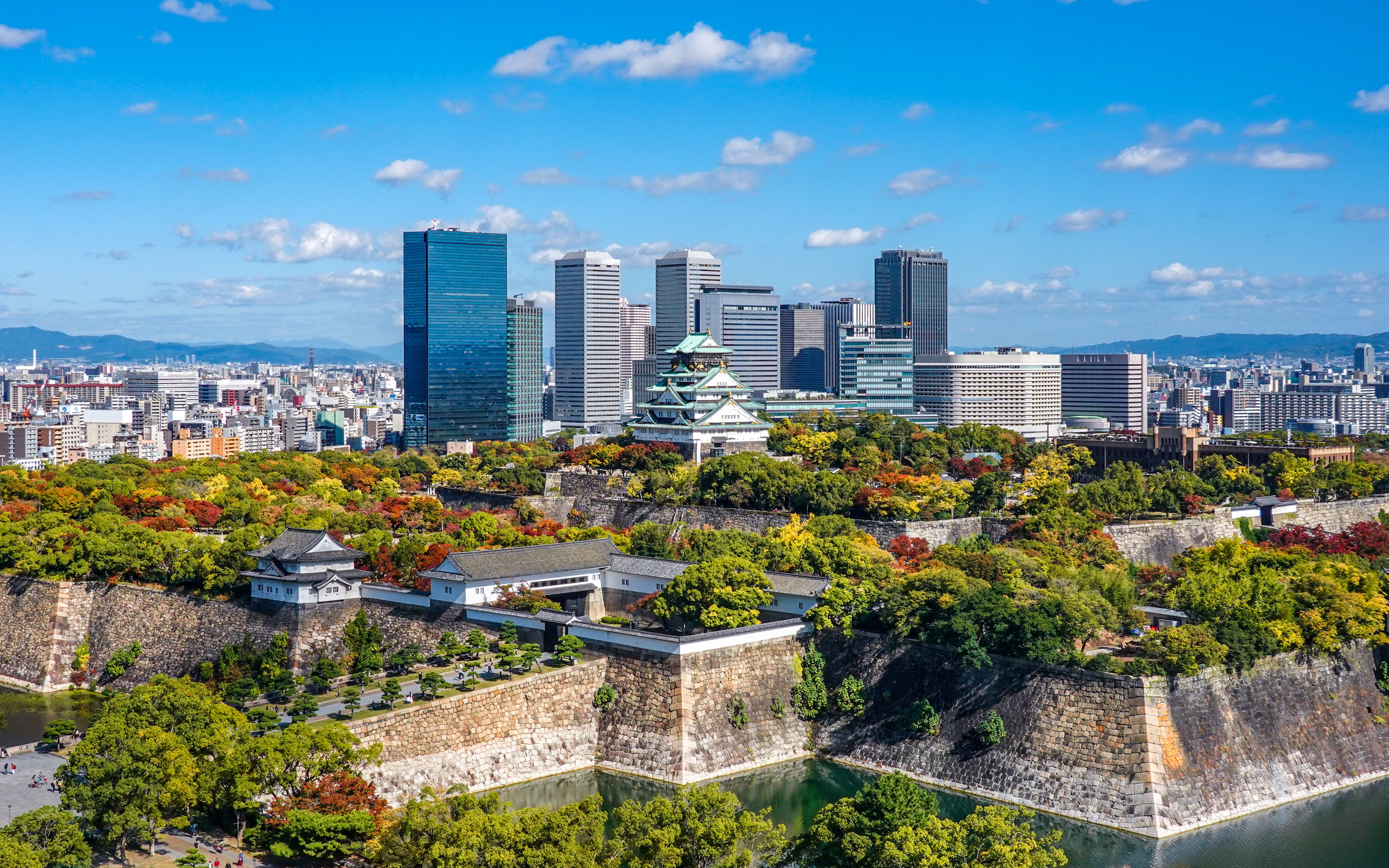 Osaka Castle surrounded by autumn foliage with city skyline in Kansai, Japan.
