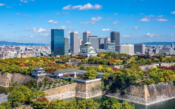 Osaka Castle surrounded by autumn foliage with city skyline in Kansai, Japan.