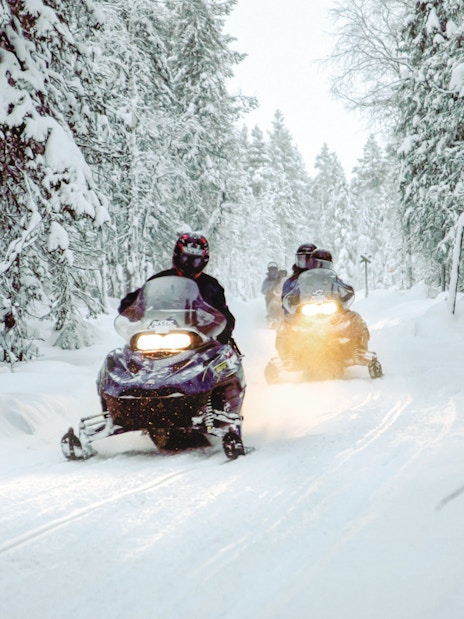 Snowmobiles driving through snowy forest in Rovaniemi during a safari.