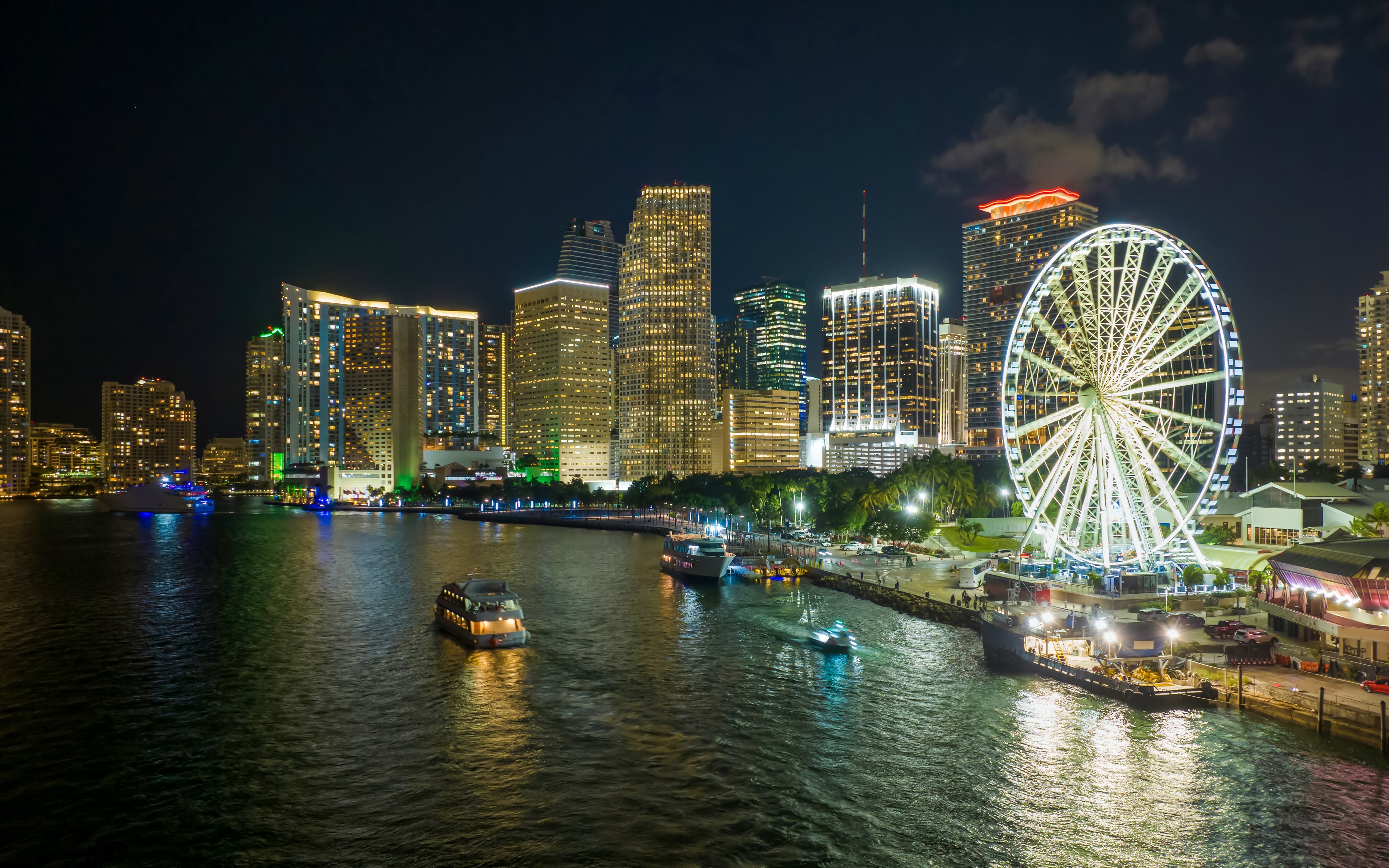 Nighttime view of Miami skyline with ferris wheel and boats on the water.