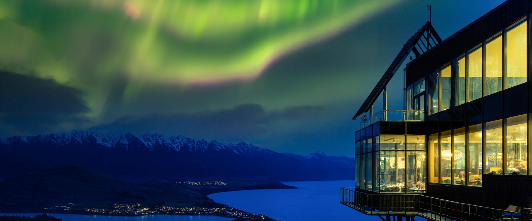 Queenstown skyline with aurora over Lake Wakatipu and mountains at night.