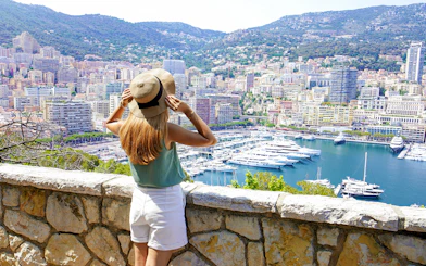 Girl overlooking Monte Carlo harbor with yachts and cityscape in view.