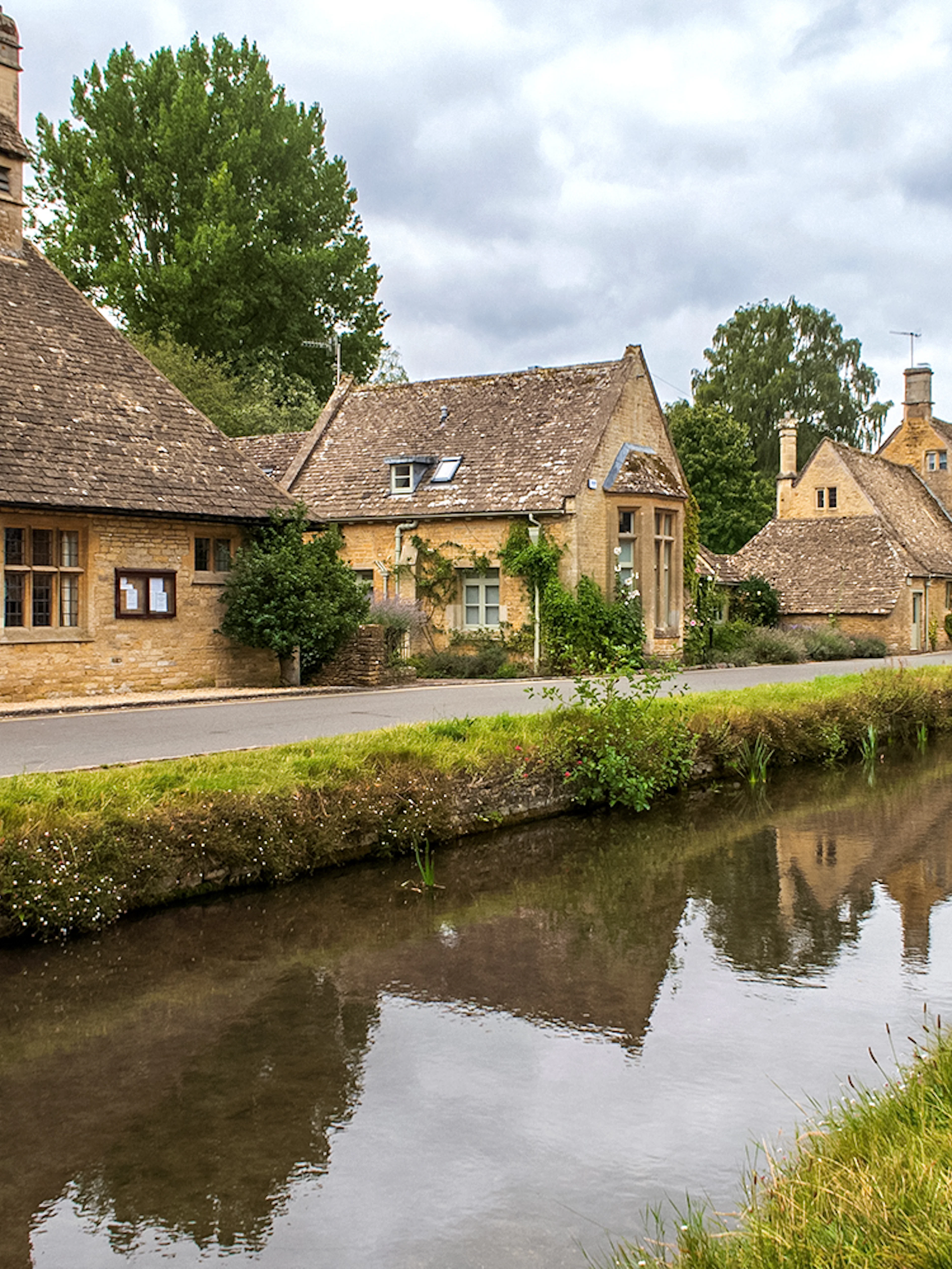 Cotswolds village street with stone cottages and canal, part of a guided day tour from London.