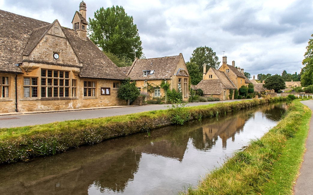 Cotswolds village street with stone cottages and canal, part of a guided day tour from London.