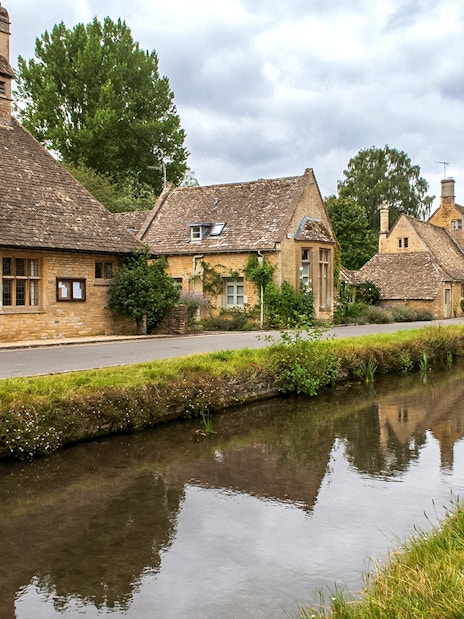 Cotswolds village street with stone cottages and canal, part of a guided day tour from London.