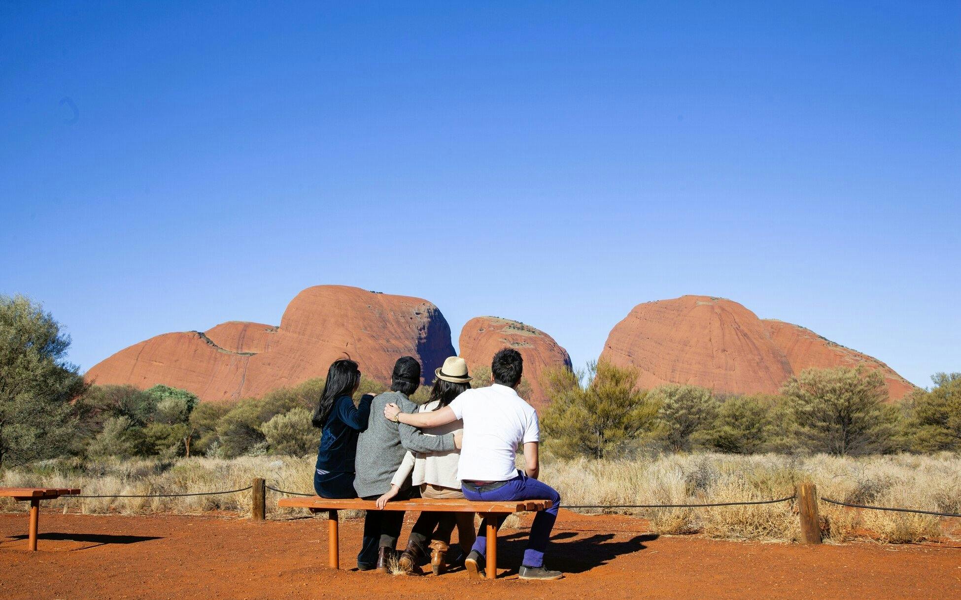 Tourists sitting on a bench viewing Kata Tjuta rock formations in the Australian Outback.