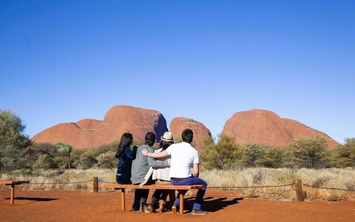 Tourists sitting on a bench viewing Kata Tjuta rock formations in the Australian Outback.