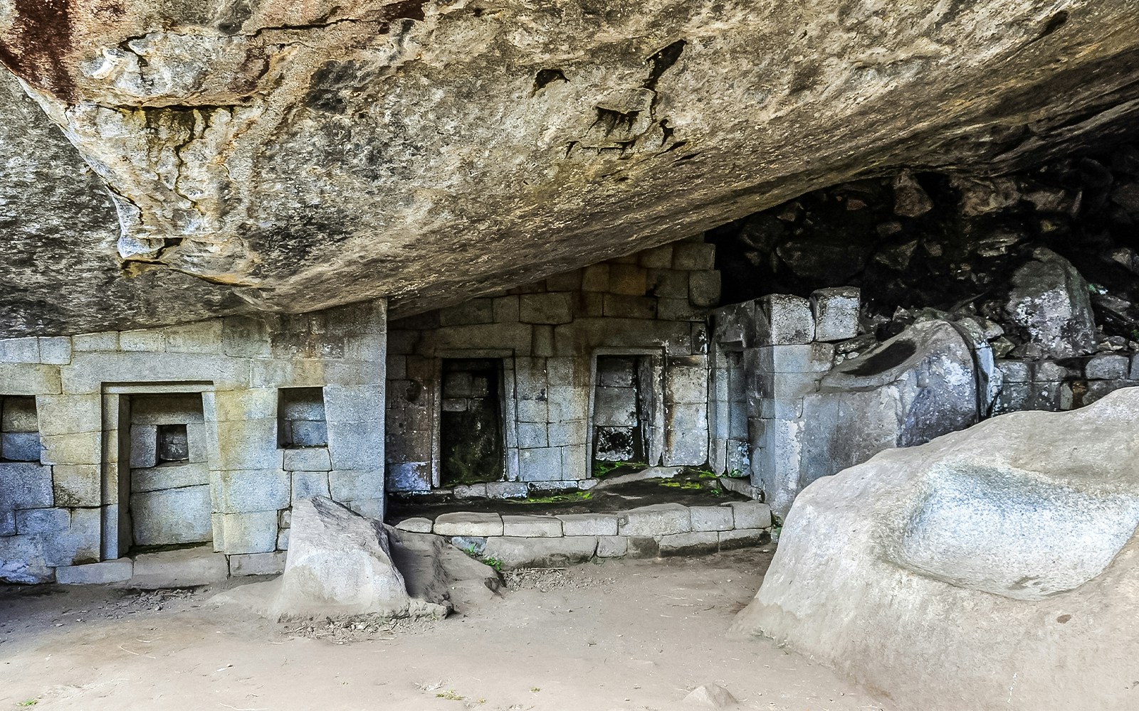 Tourists exploring the Great Cave at Machu Picchu, Peru, surrounded by ancient stone structures and lush greenery.