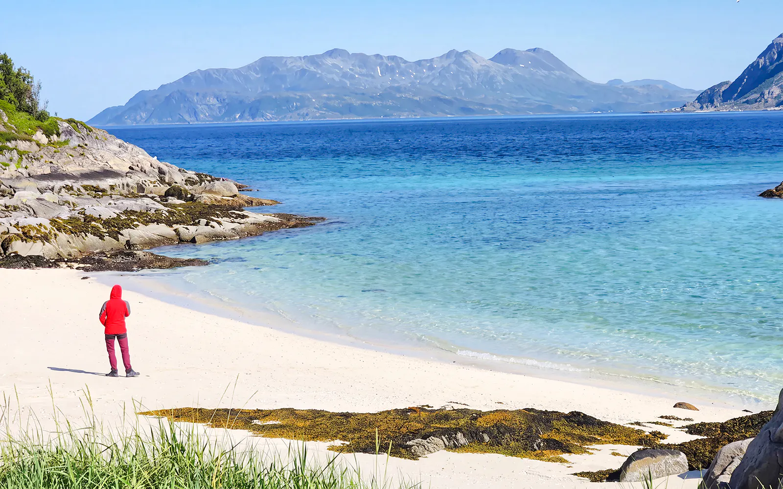 Person walking on Sommarøy beach with fjord and mountains in Tromsø, Norway.