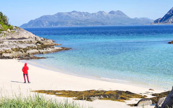 Person walking on Sommarøy beach with fjord and mountains in Tromsø, Norway.