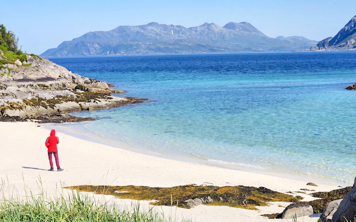 Person walking on Sommarøy beach with fjord and mountains in Tromsø, Norway.
