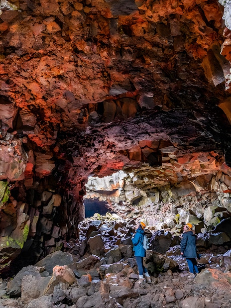 Guests exploring Raufarhólshellir Lava Cave's colorful rock formations, Iceland.